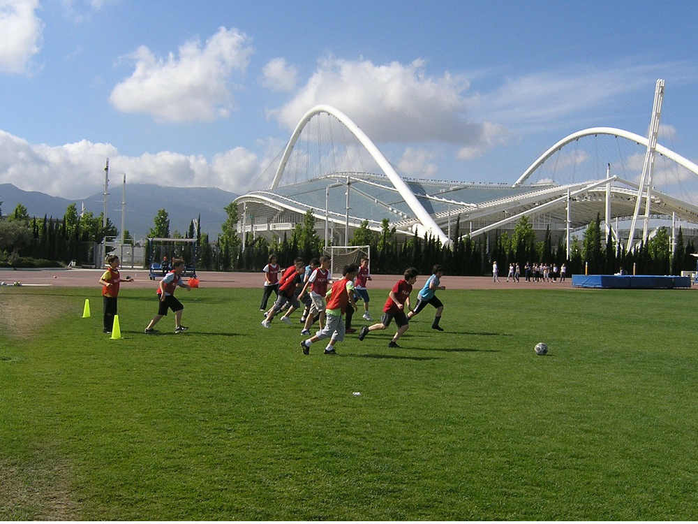 τα παιδιά στο summer camp παίζουν ποδόσφαιρο στο ανοικτό ολυμπιακών διαστάσεων γήπεδο στο οακα